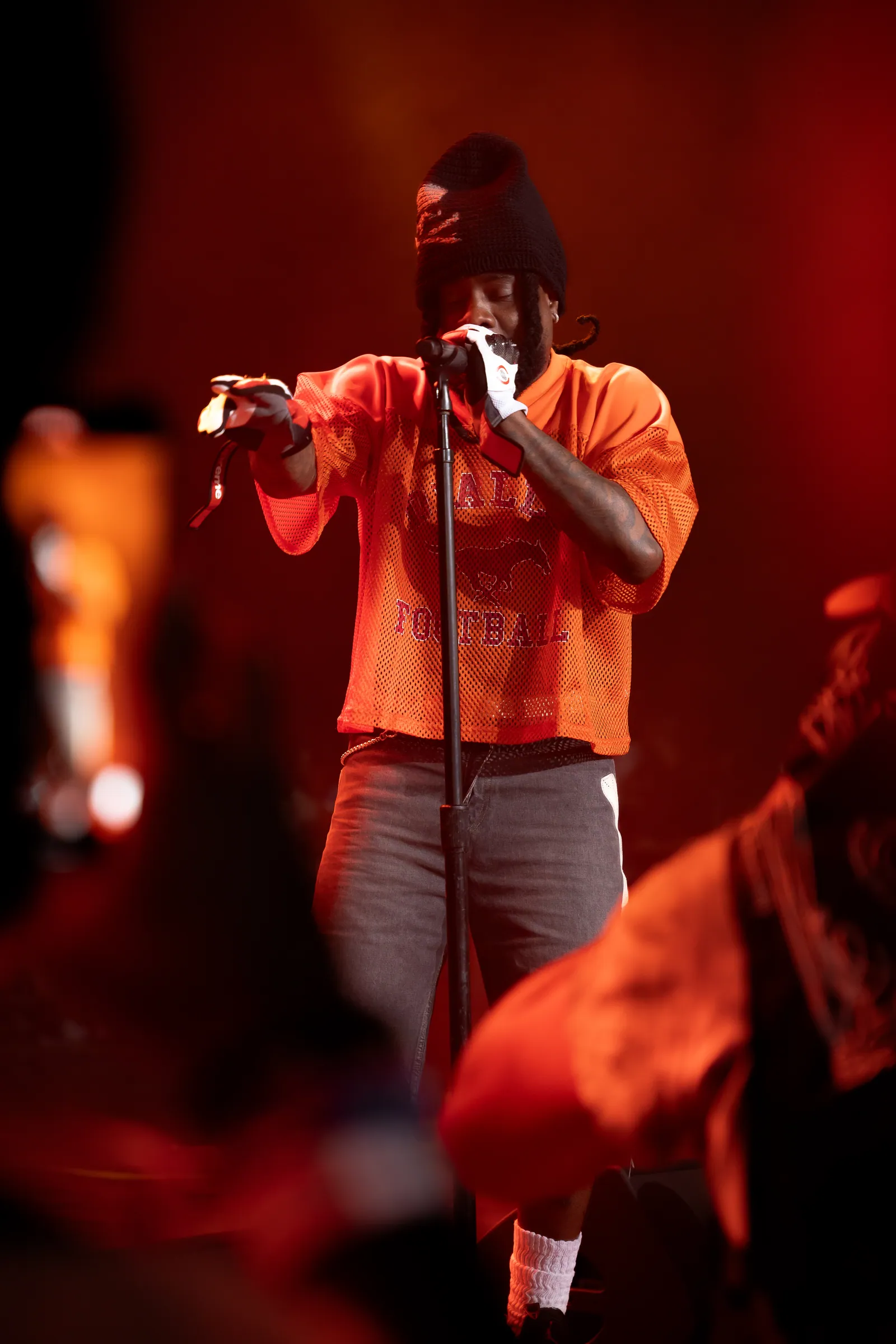 Wale performing on stage at Roots Picnic 2025, fan's camera phone visible in the foreground