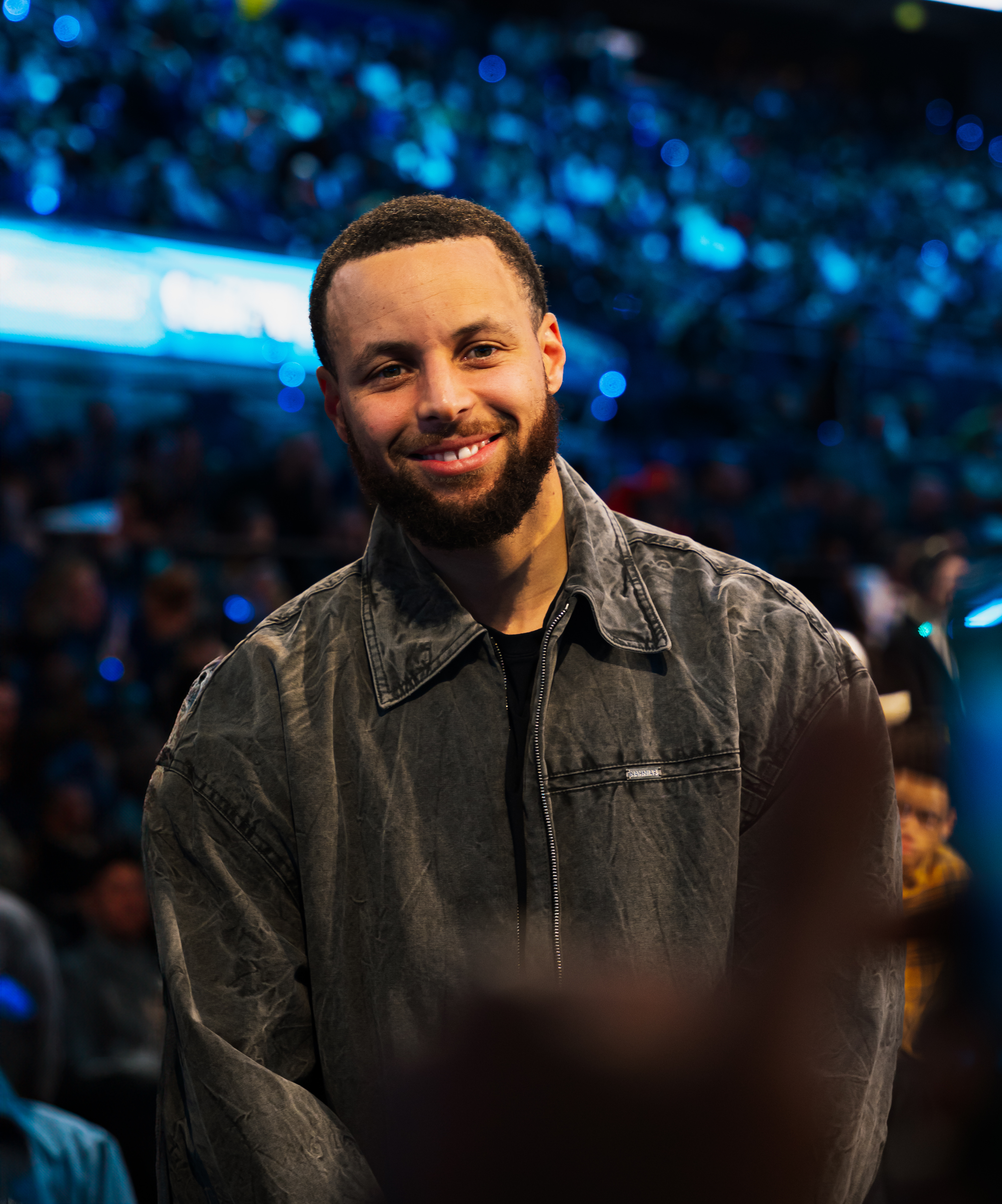 Stephen Curry smiling courtside at the 2025 NBA All-Star Game at Chase Center in San Francisco